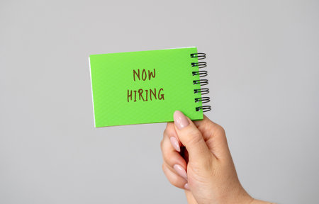Notebook with the description Now hiring in a hand. Employee Search. Attraction to work. Human Resource Management. Hire. Promotion. Working staff. Business conceptの写真素材
