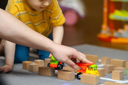 A three year old toddler boy plays with his dad blocks and cars in the children's room. Hobbies and family leisure. Spending time together. focus on wooden blocksの写真素材