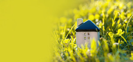 Miniature white house on a green grass. Real estate concept. Eco-friendly home. Buying a housing outside the city. Selective focus, bannerの写真素材