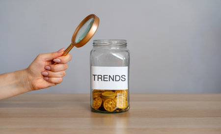 Bank of coins with the inscription Trends and magnifying glass. Analysis popular and relevant topics. New ideological trends of fashion. Recent and latest trend. Business and finance. Investmentsの写真素材