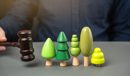 Judge's gavel in a hand and toy trees. Concept of court cases related to environmental protection and ecological problems. Natural resources. Protecting nature and environmental lawの写真素材