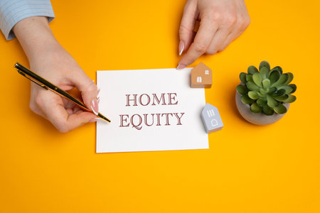 Home equity concept. Difference between the current market value of your home and the outstanding balance of any loans or mortgages secured by the property. A woman writes in notes. Real estateの写真素材