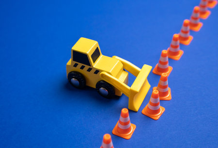 A bulldozer pushes through a border fence made of traffic cones. Waiver of rules. Breaking agreements. Revising regulations, or pushing past limitations. Disruption of norms.の写真素材