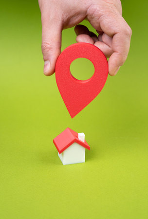 New place of residence. Hand with geolocation button points to the house. Depicts home search, real estate apps, or relocation decisions. Property selection, moving, or housing preferencesの写真素材