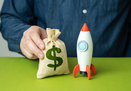 A man places a dollar money bag near a startup rocket. Startup investment. Capital injection. Venture funding. Innovation boost. Early stage projects.の写真素材