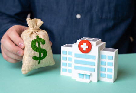 Man holding dollar money bag near hospital building. Investments in medicine, charity fund. Healthcare funding, budget.の写真素材