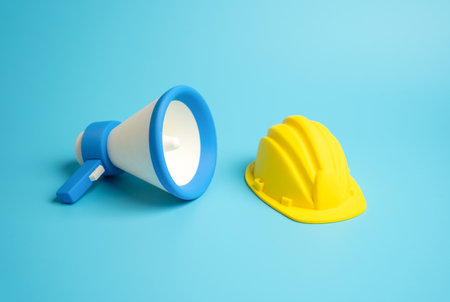 Megaphone and a hard construction helmet. Safety precautions and notifications for complex construction stages and operations. Recruiting new construction workers. Construction industry standardsの写真素材