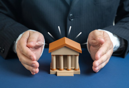 An official in a suit protects a bank building with his palms. Protecting the interests of the banking sector. Finance security, regulation and economic stability.の写真素材