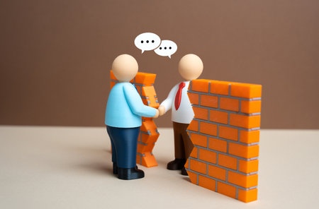 Businessmen shake hands through a gap in the wall. To break through the wall of misunderstanding. To reach a compromise. Cooperation, conflict management and cross-border partnership.の写真素材
