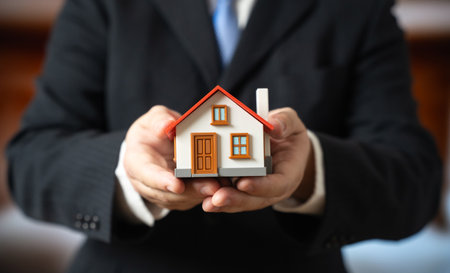 The businessman holds the house in his hands. Home ownership. Construction. Rental. Buying and investing in real estate. Mortgage, housing markets and property management.の写真素材