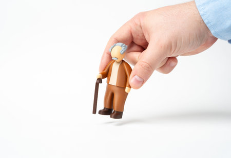 A hand places a figurine of an elderly man with a cane. Pensioners and the elderly. A figurine of a...