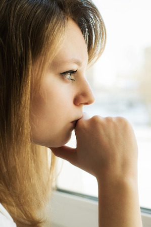 Beautiful girl thinks, looking forward, sitting at the windowの写真素材