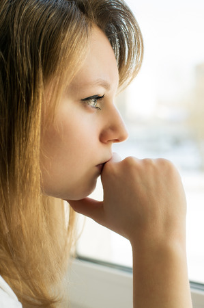 sad girl looking out the window, in the houseの写真素材