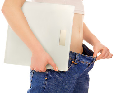 beautiful young woman with big jeans and holds the scales isolated on white backgroundの写真素材