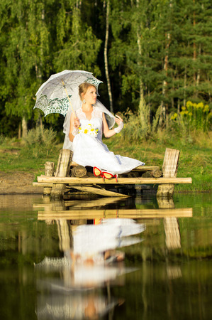 Bride with umbrella sits on a wooden bridgeの写真素材