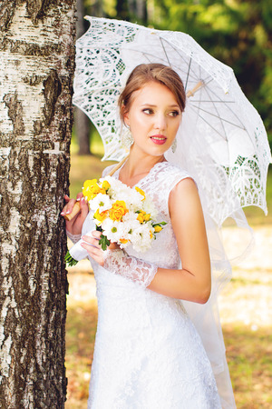 Beautiful young bride standing in the woods with umbrellaの写真素材