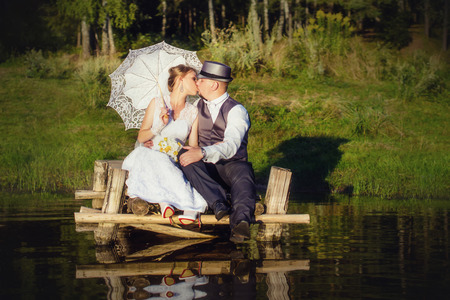 Beautiful bride with umbrella and groom kiss on the bridgeの写真素材
