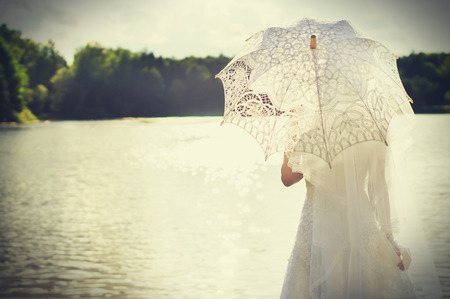 Sunset, beautiful bride with an umbrella on a background of waterの写真素材
