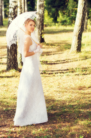 Beautiful bride walks in the forest with umbrellaの写真素材