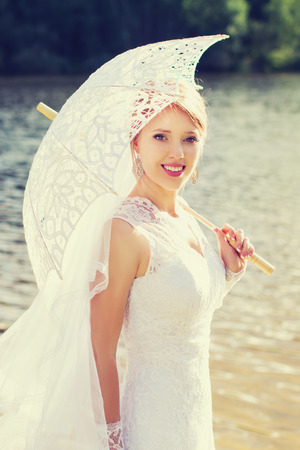 Beautiful, happy bride with an umbrella near the waterの写真素材