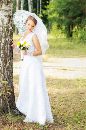 Bride with umbrella standing near a tree in the woodsの写真素材