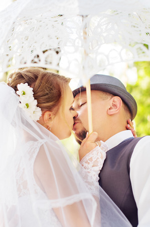 Beautiful bride and groom kissing under an umbrella on the natureの写真素材