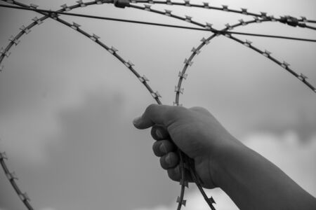 Hand of a refugee behind barbed wire
