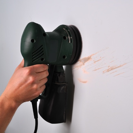 Sanding scratches on damaged wall with electric round sanderの写真素材