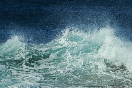 Close-up to broken wave with spray, rough surface, foam and blue ocean in backgroundの写真素材