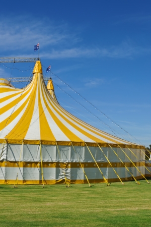 Circus tent with bright yellow and white strip?s with Australian flag on top, standing on green grass, blue sky in cornerの写真素材