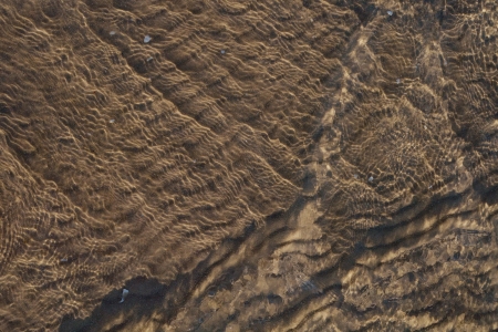 Texture of clear water over sand ripples on sea bottom with bubbles and shadows from side lightの写真素材