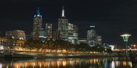Night panorama of Melbourne CBD from Yarra river with lighted platforms and trees at Flinders station with skyscrapers in background in Victoria, Australiaのeditorial素材