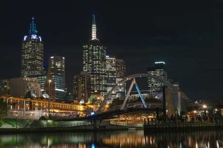 Melbourne CBD and Southbank Footbridge over Yarra River with people in cafe at Ponyfish island at night and Flinders station in background in Victoria, Australiaのeditorial素材