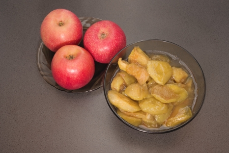Cooked apple jam with apple pieces in jar and raw fresh red apples on the plate on table