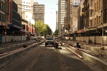 New tram platform at Elizabeth street prepared with communication pipes and wires with several workers on construction site, stack of pipes and small track in the middle of the street with bright light on buildings in background on October 7, 2013のeditorial素材