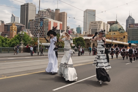 Three ladies in costumes walking on stilts on Emirates Melbourne Cup Parade with musicians and Flinders Street building in background on November 4, 2013 in Melbourne, Australiaのeditorial素材