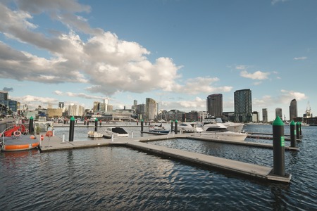 Pier with several different boats moored in Docklands with Melbourne city skyline and clouds on blue sky in backgroundのeditorial素材