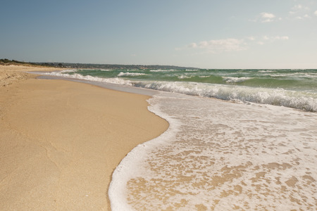 Breaking wave curve on sandy beach in motion with bubbles, splashes, coastline and light clouds over blue skyの写真素材