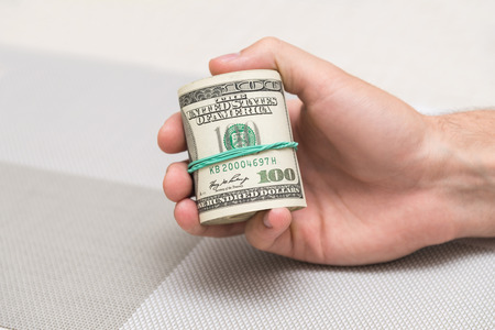 A man holds a bundle of money in his hand tied with an elastic bandの写真素材