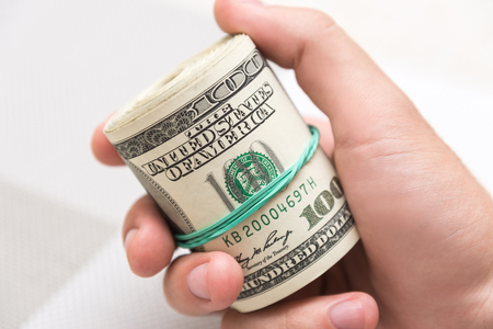 A man holds a bunch of money, twisted in a bunch and tied with a green rubber band on a light textured backgroundの写真素材