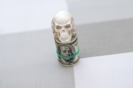 A skull standing on a bundle of money, twisted in a bunch and tied with a green rubber bandの写真素材