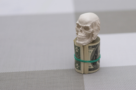 A skull standing on a bundle of money, twisted in a bunch and tied with a green rubber bandの写真素材