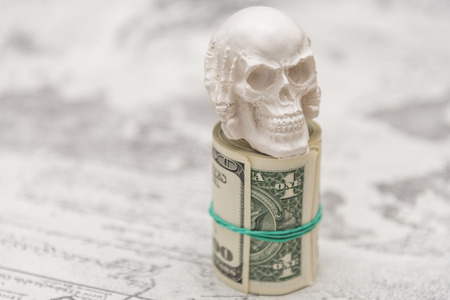 A skull standing on a bundle of money, twisted in a bunch and tied with a green rubber bandの写真素材