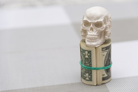 A skull standing on a bundle of money, twisted in a bunch and tied with a green rubber bandの写真素材