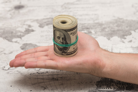 A man holds a bunch of money, twisted in a bunch and tied with a green rubber band on a light textured backgroundの写真素材