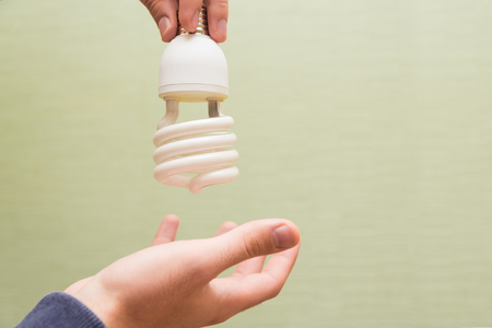 Energy saving light bulb in the hands of a man on a light backgroundの写真素材