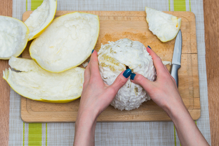 Girl cleans a pomelo on a wooden boardの写真素材