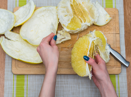 Girl cleans a pomelo on a wooden boardの写真素材