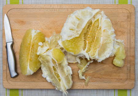 Cleansed pomelo and knife lying on a wooden boardの写真素材