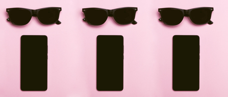 Black glasses. Black phone. Pink background. Black phone and glasses are lying on a pink background.の写真素材